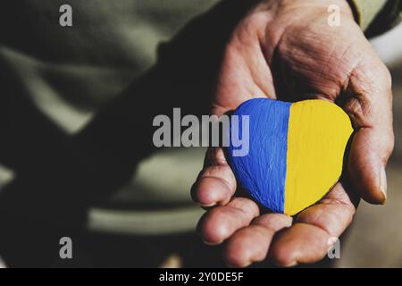 Hommes ou soldats âgés mains tenant coeur pierre peinte avec les couleurs du drapeau national de l'Ukraine. Priez pour l'Ukraine, arrêtez la guerre, sauvez le peuple d'Ukraine a Banque D'Images