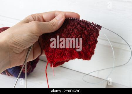Fil coloré brillant avec crochet tricoté et aiguilles dans les mains fils dégradés lumineux avec beau motif. Crochet rouge et violet sur blanc Banque D'Images