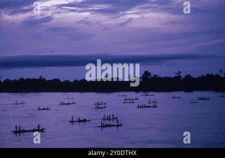 Les gens dans de grands canoës ou pirogues pagayent chez eux sur le fleuve Congo au crépuscule. Banque D'Images