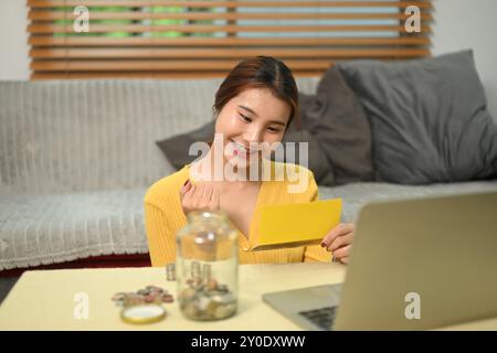 Jeune femme regardant le livret de banque avec une expression heureuse, réalisant un jalon d'épargne Banque D'Images