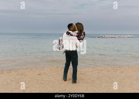 Mari et femme diversifiés embrassent sur la plage tout en embrassant Banque D'Images
