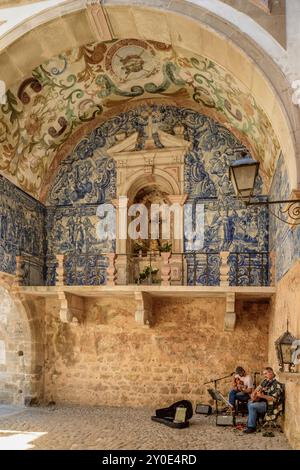 Un couple d'artistes de rue jouant de la guitare et chantant dans la voûte de la porte principale de la ville fortifiée d'Obidos, au Portugal. Décoration carrelage. Banque D'Images