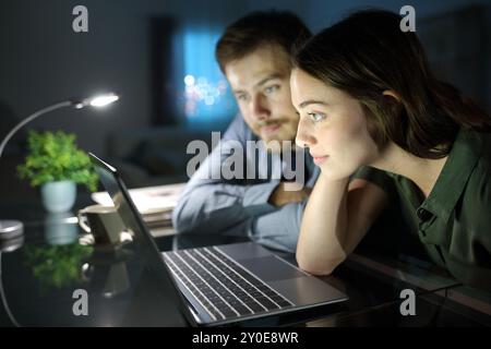 Couple sérieux regardant le contenu d'un ordinateur portable dans la nuit à la maison Banque D'Images