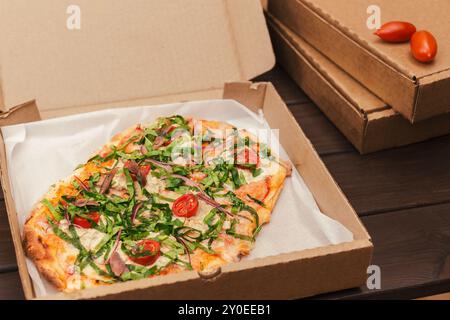 Pizza italienne garnie d'anchois, câpres, oignon rouge dans une boîte de livraison ouverte, avec des boîtes en carton empilées à proximité Banque D'Images