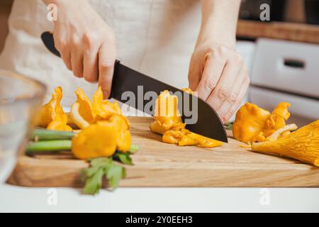 Gros plan mains hachant v chanterelles jaunes champignons sur une planche à découper en bois, préparant un plat de dîner végétarien aux champignons Banque D'Images