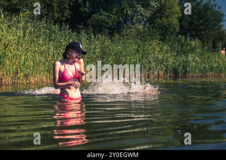 Femme ludique éclaboussant de l'eau dans le lac heureux été Banque D'Images
