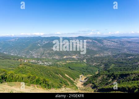 Un pont routier courbe au fond d'un abîme, un village sur une pente, des montagnes, la crête du Caucase couverte de nuages Banque D'Images