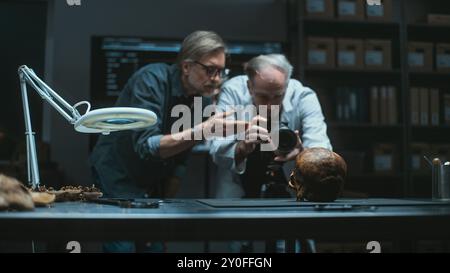 Deux archéologues photographient des restes fossiles d'un ancien crâne humain avec un appareil photo professionnel sur trépied, discutent. Scientifiques ou historiens travaillent dans un laboratoire archéologique moderne. Concept archéologique Banque D'Images