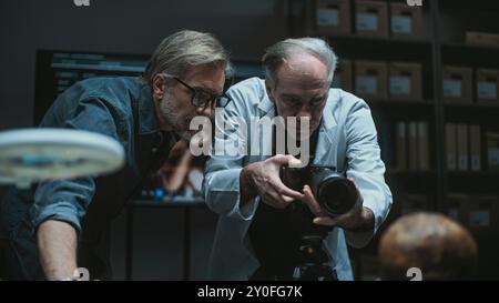 Deux archéologues parlent et prennent des photos de restes fossiles du crâne humain préhistorique en utilisant un appareil photo professionnel sur trépied. Les scientifiques travaillent dans un laboratoire archéologique moderne. Concept d'archéologie. Banque D'Images