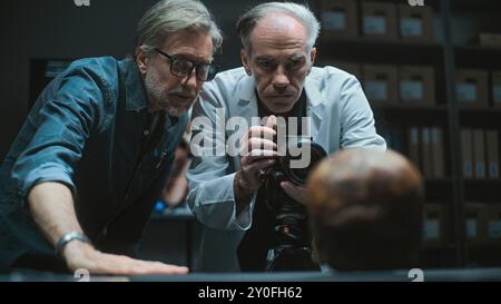 Laboratoire archéologique moderne : deux archéologues ou scientifiques photographient une collection de spécimens fossiles de squelette humain préhistorique avec un appareil photo professionnel sur trépied, discutent. Concept archéologique Banque D'Images