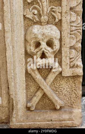 Crâne et os croisés sculptés dans la pierre ; baroque Monopoli Cathédrale monopoli italie avec squelettes de cardinaux, la porte en bois, crânes en pierre sculptés et l'intérieur Banque D'Images