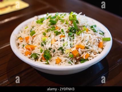 Gros plan de riz frit aux légumes dans un bol en céramique blanche. Table en bois. Banque D'Images