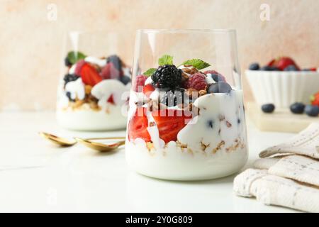 Yaourt savoureux avec baies fraîches, granola et menthe dans des verres servis sur une table blanche Banque D'Images