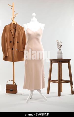 Un mannequin féminin avec robe, rack avec veste, tabouret, fleurs de coton et sac sur fond clair Banque D'Images