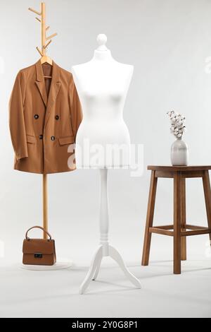 Un mannequin féminin, rack avec veste, tabouret, fleurs de coton et sac sur fond clair Banque D'Images