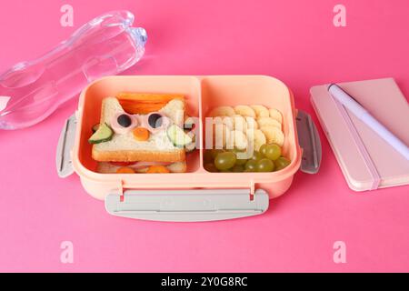 Boîte à lunch avec collations, bouteille d'eau et papeterie sur fond rose Banque D'Images