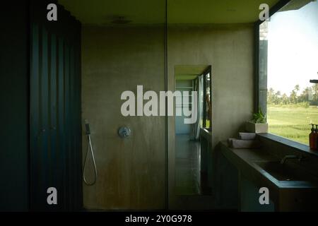 Tabanan, Bali, Indonésie - 26 août 2024 : design minimaliste industriel de salle de bain avec une douche, un grand miroir et un lavabo avec des finitions en béton ov Banque D'Images