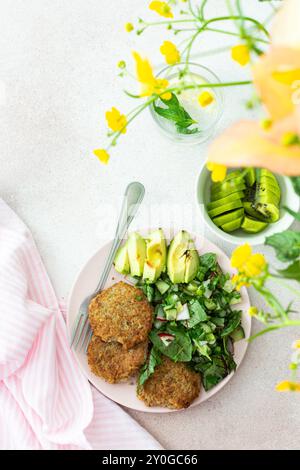 Côtelettes de quinoa et salade mixte avec avocat et radis, kiwi et eau avec citron, délicieux petits déjeuners copieux, une table avec de la nourriture et un vase de Banque D'Images