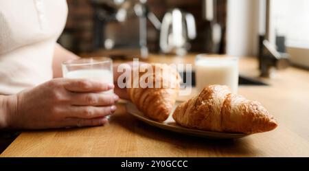 Fille a un petit déjeuner avec du lait et des croissants à la cuisine. Femme avec latte bio blanc et pâtisserie française Banque D'Images