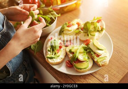 Mains de fille préparant des sandwichs avec avocat, légumes et légumes verts à la cuisine. Bruschettas végétariens avec légumes frais et roquette Banque D'Images