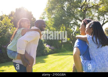 Porter des filles piggyback, parents multiraciaux souriants et profiter du temps en famille dans le parc ensoleillé Banque D'Images