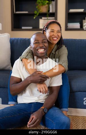 Couple multiracial souriant assis sur le sol, embrassant et profitant du temps ensemble à la maison Banque D'Images