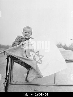 Un enfant de cinq ans est assis sur une jeep américaine tenant un drapeau Star of David juste avant son départ de Buchenwald pour la France. Le garçon a été identifié comme Briner Odon , dont la mère et le père ont été abattus par les nazis. Il fait partie d'un groupe d'orphelins juifs libérés du camp de concentration de Buchenwald et envoyés en France. De là, certains voyageront en Palestine et d'autres en Amérique. Banque D'Images