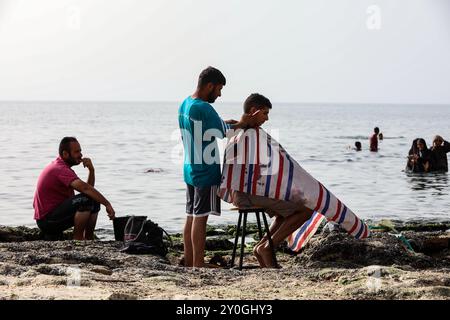 Deir al-Balah, bande de Gaza, Palestine. 20 mai 2024. Un palestinien se fait couper les cheveux sur une plage près de Deir al-Balah, au centre de la bande de Gaza, qui est en proie à des assauts. Malgré plus de sept mois de violents bombardements israéliens et aucun endroit sûr dans l'enclave palestinienne, les habitants de Gaza visitent le front de mer pour un bref répit après la guerre et la chaleur intense de leurs tentes de fabrication voisines Banque D'Images