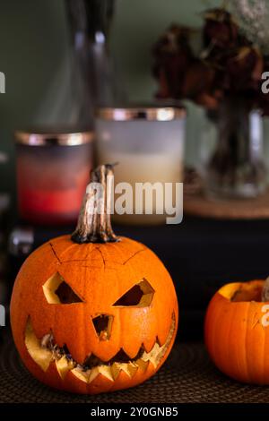 Citrouille sculptée avec des bougies parfumées et un vase à fleurs dans le fond flou. Thème d'Halloween Banque D'Images