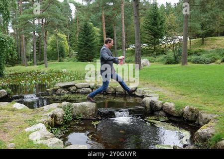 Un homme saute par-dessus un ruisseau dans un parc en Norvège Banque D'Images