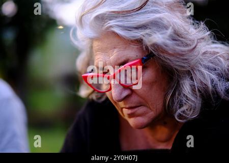 Femme aînée réfléchie avec les cheveux gris et les lunettes de chat rouge respire l'élégance et la sagesse dans un portrait en gros plan Banque D'Images