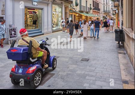 Sitges, Barcelone-01 septembre 2024 : scène urbaine dynamique à Sitges, Barcelone, avec une personne en fauteuil roulant électrique naviguant dans une rue remplie Banque D'Images