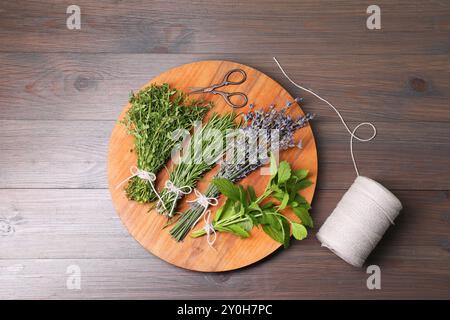 Différentes herbes aromatiques, fil et ciseaux sur table en bois, vue de dessus Banque D'Images