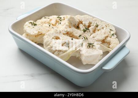 Steaks de chou-fleur non cuits avec des épices dans un plat de cuisson sur une table en marbre blanc, gros plan Banque D'Images