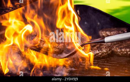 Cuisson de hamburgers sur un gril chaud avec des flammes - galettes hamburger de style barbecue dans la cour arrière grillées à la flamme. Les hamburgers sont un barbecue traditionnel d'été en plein air. Banque D'Images