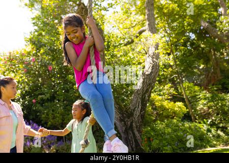 Jouant dehors, fille se balançant sur la corde pendant que la famille regarde dans le jardin Banque D'Images