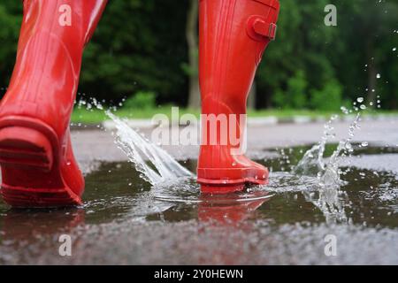 Femme portant des bottes en caoutchouc rouges marchant dans une flaque d'eau à l'extérieur, gros plan Banque D'Images