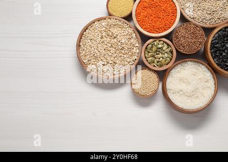 Différents types de céréales, graines et légumineuses dans des bols sur une table en bois blanc, pose à plat. Espace pour le texte Banque D'Images