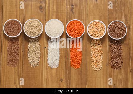 Différents types de céréales et de légumineuses dans des bols sur une table en bois, pose à plat Banque D'Images