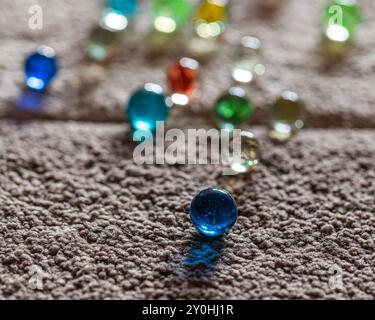 Marbres colorés dispersés sur un tapis texturé, se concentrant sur un marbre bleu singulier Banque D'Images