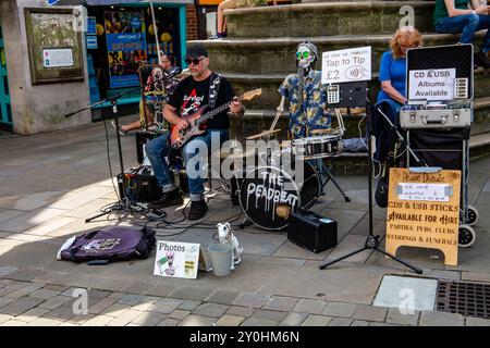 Artiste de rue jouant de la musique dans un cadre urbain animé, mettant en vedette un batteur squelette et divers panneaux publicitaires conseils et ventes de CD. Banque D'Images