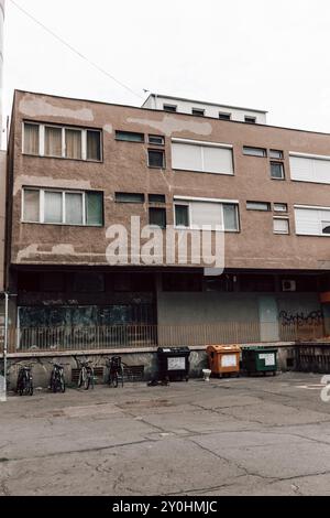 Poubelles pour les ordures et les ordures à côté des vélos stationnés pour les cyclistes sous un immeuble d'appartements dans une rue résidentielle calme à Szeged, Hongrie. Banque D'Images