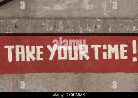Lettrage blanc peint sur fond rouge, encourageant les téléspectateurs à prendre leur temps Banque D'Images