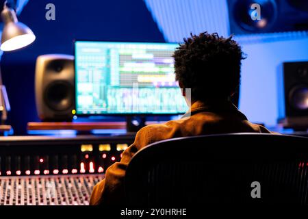 Compositeur de disques afro-américain mixant et mastering des chansons avec un logiciel audio, travaillant avec des curseurs automatiques et des boutons pour régler les niveaux de volume sonore. Ingénieur du son créant de nouvelles musiques. Banque D'Images