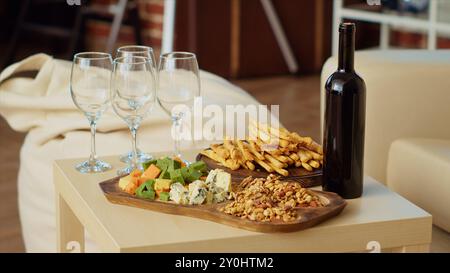 Gros plan du plateau de charcuterie et du plateau de fromage gastronomique mis en place par les hôtes pour accueillir correctement les invités arrivant bientôt à la fête de l'appartement. Bouteille de vin et verres à côté des hors-d'œuvre dans le salon Banque D'Images