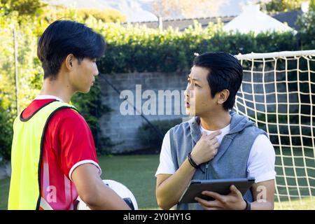 Entraîneur tenant une tablette discutant de stratégie avec un adolescent joueur de football tenant le ballon sur le terrain Banque D'Images