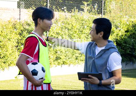 Entraîneur encourageant le jeune joueur de football masculin adolescent tenant le ballon pendant la session d'entraînement Banque D'Images