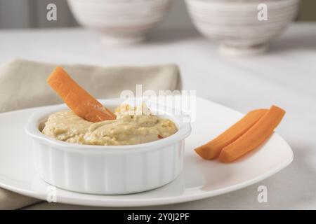 Tremper un bâton de carotte dans un bol de houmous délicieux et sain Banque D'Images