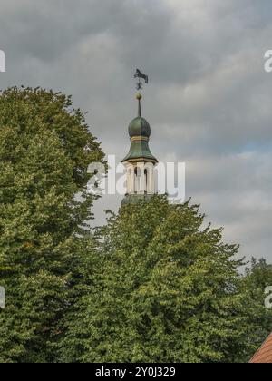 La tour de l'église s'élève au-dessus d'arbres verts denses, ciel nuageux, atmosphère historique et apaisante, dornum, frise orientale, allemagne Banque D'Images