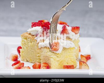 Une photo en gros plan d'une tranche de gâteau éponge maison garnie de crème fouettée et coupée de srtawberries avec une fourchette coupant dedans Banque D'Images